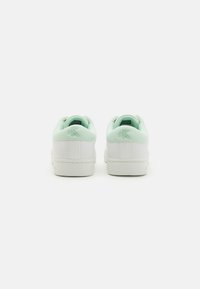 Hvite sneakers med mintgrønn akcent ved hælene. Glatt skinn øvre, polstret krage og flat gummisåle. Enkel design.