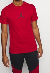 Rode katoenen T-shirt met korte mouwen, voorzien van een grijze Jumpman-logo in het midden. Gedirigeerd met zwart-rood gemusterde broek.