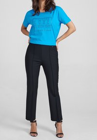 Niebieska koszulka z krótkim rękawem z czarnym nadrukowanym tekstem; w zestawieniu z dopasowanymi czarnymi spodniami z detalami szwów i prostym krojem nogawek. Czarne sandały na obcasie.