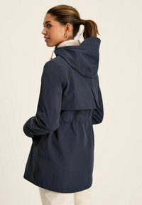 Jūras spēku ūdensnecaurlaidīga jaka ar stiprinājumu kapuci, elastīgu jostu un slāņotu aizmugures dizainu. Iezīmējas ar gaišas krāsas iekšpusi un sānu kabatām.