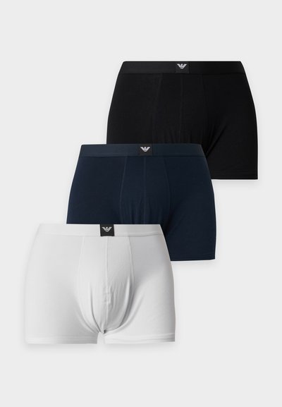 Trois paires de boxers pour hommes en noir, bleu marine et blanc, chacun avec un petit logo au centre avant de la ceinture.