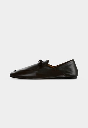 Μαύρο δερμάτινο μοκασίνι slip-on με μικρή λουρίδα στο πάνω μέρος, εμφανίζεται σε πλαϊνή όψη σε απλό φόντο.