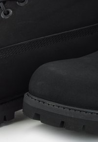 Botas de ante negro con puntera redondeada, suela de goma gruesa y detalle de costura en contraste a lo largo de los lados.