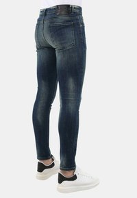 Skinny-fit jeans van donkerblauw denim, met vervaging op de dijen, een zwarte leren patch op de tailleband en vijf zakken, gecombineerd met witte sneakers.