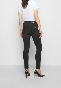 Black skinny jeans with a high waist, featuring a subtle design on the back pockets, paired with a white t-shirt and black heels.