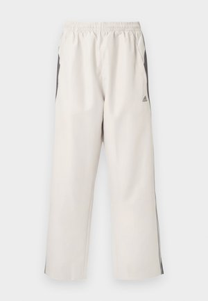 Lichtbeige trainingsbroeken met een elastische taille, zijzakken, zwarte zijstrepen en een Adidas-logo op de linker bovenbeen. Glad textuur van de stof.
