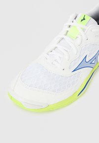 Λευκό αθλητικό παπούτσι με πάνω μέρος από δίχτυ, μπλε λεπτομέρειες και νεον πράσινο σχέδιο στη σόλα. Διαθέτει κλείσιμο με κορδόνια και υλικά με υφή.