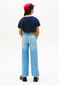T-shirt blu navy, jeans a gamba larga blu chiaro, cappellino rosso e blu, scarpe nere, etichetta del brand visibile sui jeans. Texture liscia, design casual.