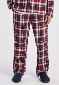 Rode en groene geruite pyjamabroek van zachte stof, met een relaxte pasvorm en een wit T-shirt, gecombineerd met marineblauwe slippers.