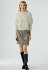 Pull en maille côtelée blanche avec des épaules tombantes, associé à une jupe pied-de-poule noir et blanc. Des bottes noires à hauteur de genoux complètent la tenue.