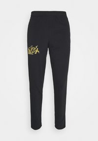 Svarta sweatpants i bomullsblandning med en åtsittande design och elastisk midja. Guldlejonmönster på vänstra låret ger extra detaljer.