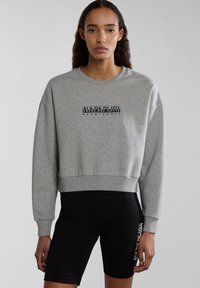 Grijze cropped sweatshirt met ribbelboorden en onderrand, met een zwart logo-ontwerp in het midden. Gecombineerd met zwarte shorts.