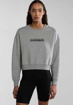 Grijze cropped sweatshirt met ribbelboorden en onderrand, met een zwart logo-ontwerp in het midden. Gecombineerd met zwarte shorts.