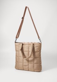 Beige puffer tote soma ar quiltotu dizainu, kas aprīkota ar divām šūtu rokturiem un noņemamu regulējamu plecu jostu. Mīksta tekstūra.