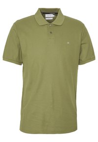 Polo vert olive en coton, doté d'un col, d'une patte à trois boutons, et d'un logo brodé subtil sur le côté gauche de la poitrine.