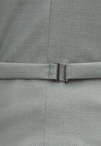 Grauer strukturierter Stoff mit einem Diamantmuster, versehen mit einem glatten Wickelgürtel, der mit einer rechteckigen Metallschnalle gesichert ist.