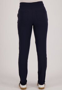 Marineblauwe tapse broek van zachte stof, met een hoge tailleband, twee achterzakken en een subtiele glans. Witte schoenen zichtbaar aan de onderkant.