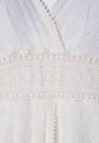 Abito di pizzo bianco con motivi floreali, tessuto testurizzato e rifiniture in pizzo. Il design presenta un collo a V e dettagli a strati.