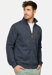 Navy zip-up sweatshirt med høj krave, struktureret strikstof, elastiske manchetter og et lille logo. Har et lynlås-hoved i brunt læder.