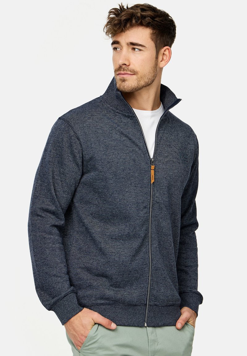 Navy zip-up sweatshirt med høj krave, struktureret strikstof, elastiske manchetter og et lille logo. Har et lynlås-hoved i brunt læder.