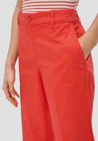Czerwone bawełniane spodnie z zapięciem na guzik, kieszeniami bocznymi i luźnym krojem. Materiał ma gładką fakturę z widocznymi detalami przeszyć.