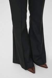 Mustad rõivastega püksid, millel on laienev lõige, kombineeritud teravate pruunide kontsadega. Materjal paistab sile ja viimistletud.