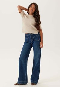 Beige ribbad stickad t-shirt med kort ärm i kombination med högmidjade, vida blå denimjeans, med framfickor och klassisk skärning.