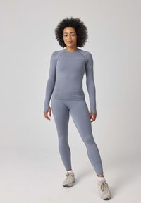 Lichtgrijs sporttop met lange mouwen en leggings van rekbare stof. Opvallende duimopeningen bij de manchetten en getextureerde panelen langs de romp.