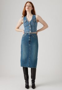 Denim crop top met knopen, V-hals, gecombineerd met een blauw denimrok met hoge taille. Model draagt kniehoge zwarte laarzen.