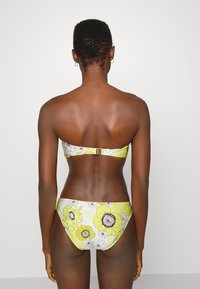 Biquíni floral amarelo com parte de cima sem alças e parte de baixo correspondente. Feito de tecido texturizado com fecho nas costas e padrões vibrantes de flores.