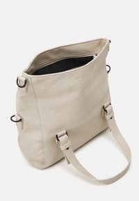 Beige Einkaufstasche mit texturierter Oberfläche, schwarzem Reißverschluss und verstellbaren Trägern. Verfügt über seitliche Ringe für zusätzliche Funktionalität.