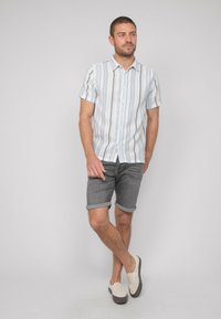Chemise à manches courtes avec des rayures verticales bleues et blanches, associée à des shorts en denim retroussés et des chaussures slip-on beiges.