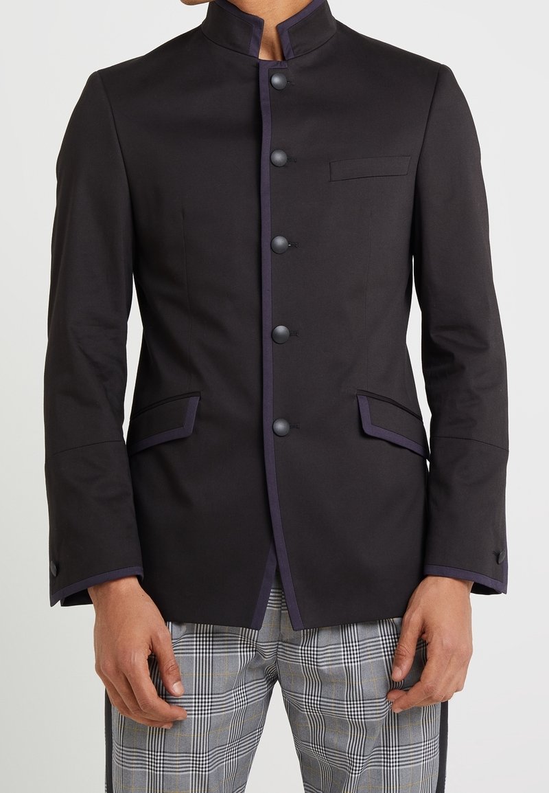 Black tailored jacket with a stand collar, purple trim, five black buttons, and two front pockets. Worn over gray plaid trousers.
