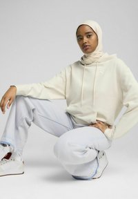 Bež hoodie s vezicom, svijetlosive široke traperice s iščupanom rubom i bijele tenisice s bordo akcentima. Mekani materijal i opušteni kroj.