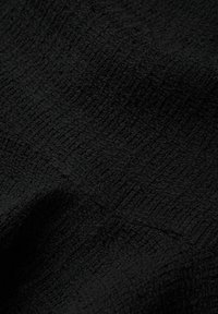Tissu noir avec un motif texturé en nid d'abeille à croisillons, présentant de légers plis et une certaine profondeur.