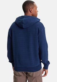 Felpa con cappuccio blu navy con cappuccio regolabile ampio, polsini e orlo a costine; tessuto strutturato, taglio morbido e cuciture minimali.