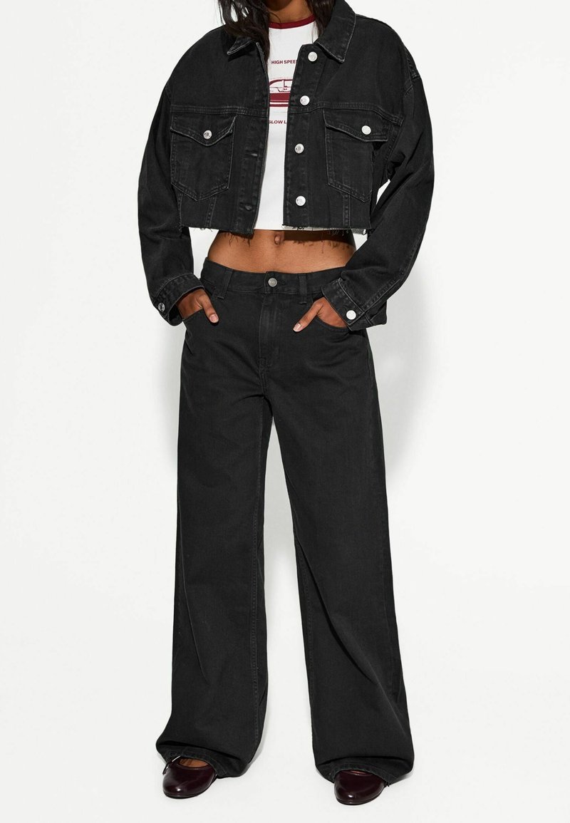 Černá zkrácená denimová bunda s knoflíkovým zapínáním a dvěma náprsními kapsami, spárovaná s černými širokými kalhotami, obě v hladké textuře.