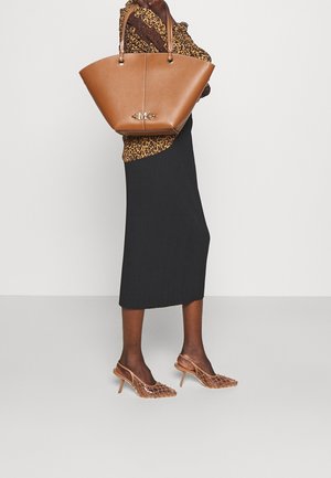 Kvinde iført leopardmønstret top og sort nederdel, bærende en stor tanfarvet håndtaske, iført brune slingback-hæle med mesh.