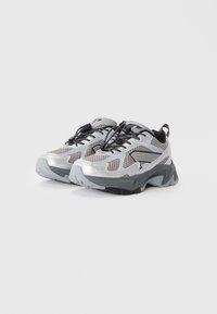 Silver athletic shoes with a mesh upper, black accents, a thick, textured sole, and black laces. Features a pull tab at the back.