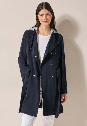Trench-coat marine avec une capuche en polaire grise, design à double boutonnage et taille nouée, comportant des boutons argentés et une texture lisse.