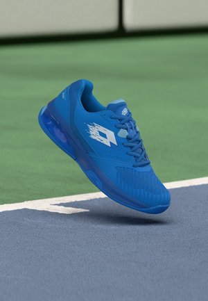 Blå atletisk joggesko med hvitt logo i luften over en tennisbanes linje, som blander grønne og blå baneflater.