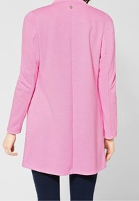 Vaaleanpunainen pitkähihainen takki, jossa on teksturoidut pinnat, takasauma ja pyöreä kultapainike kauluksessa. Slim fit -muotoilu, jossa on kaareva helma.