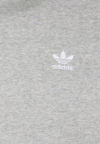Tela gris con el logo bordado de Adidas en blanco que presenta el trébol y texto en el lado central-derecho del material.