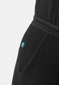 Schwarz fleeceähnliches Kleidungsstück mit einem strukturierten Bund und einer kleinen schwedischen Flagge, die an der Seite gestickt ist.