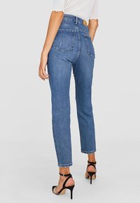 Höga midjebyxor i blå denim med rak passform, lätt blekning, två bakfickor och ankellängd, i kombination med svarta remsandaler.