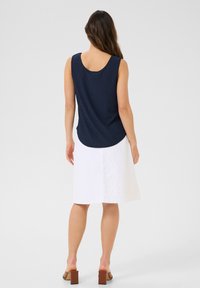 Top sans manches navy à motif texturé, associé à une jupe blanche longueur genoux et des sandales à talons blocs marron, vu de l'arrière.