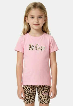 Jeune fille aux longs cheveux blonds portant un t-shirt rose Lee Cooper et un short à motif léopard, faisant face à l’avant avec une expression neutre.