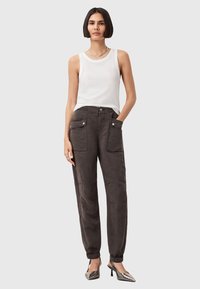 Pantaloni grigio scuro, dalla vestibilità comoda, con due tasche frontali e polsini elasticizzati. Indossati con una blusa bianca senza maniche e tacchi argento.
