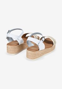 Sandalias de plataforma blancas con suela de yute trenzado, tira ajustable en el tobillo y plantilla suave de color marrón. Acentuadas con detalles metálicos.
