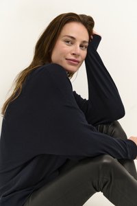 Navy oversized sweater with ribbed cuffs, paired with black leather pants. Hair is loose, giving a relaxed appearance against a plain background.
